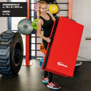 Frau trägt rote eyepower Weichbodenmatte gefaltet mit Tragegriff im Fitnessraum. Dicke Gymnastik- & Sportmatte.