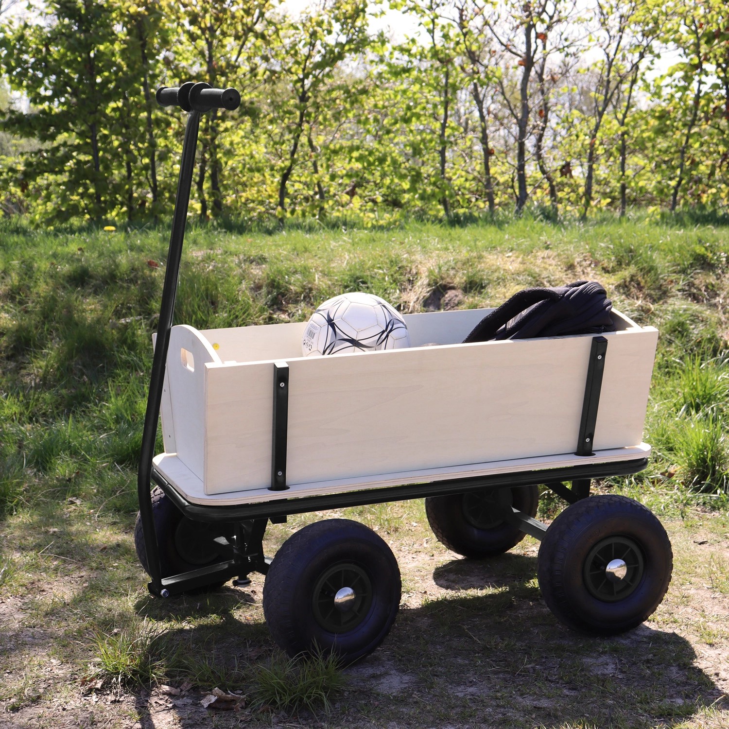 Schwarzer Sunny Bollerwagen Billy Beach Wagon mit Luftreifen, Holzkorpus und Fußball im Garten.