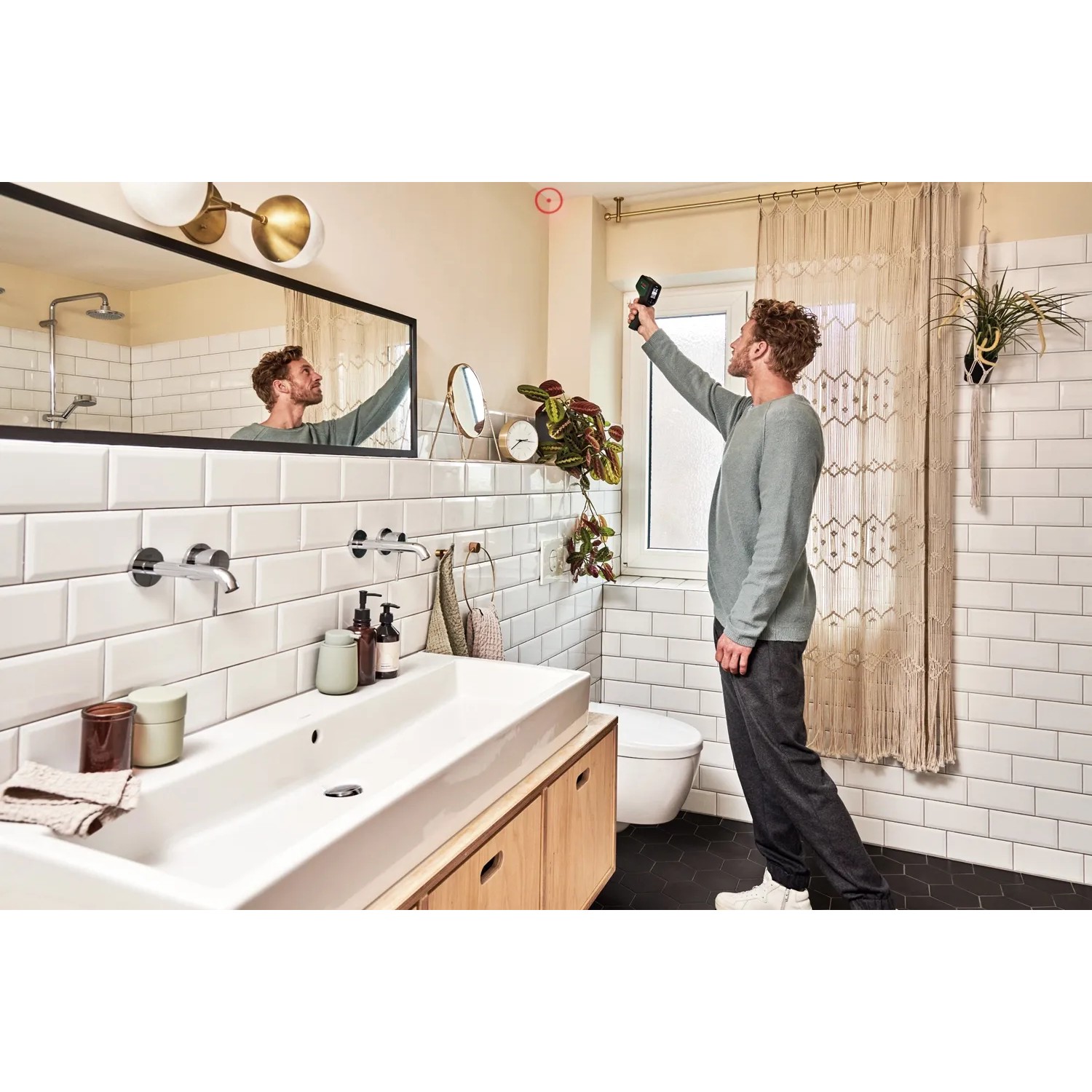 Mann misst mit Bosch AdvancedTemp Infrarot-Thermometer Temperatur im Badezimmer.
