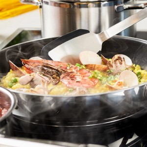 RÖSLE Elegance Bratpfanne 28 cm mit Paella und Servierhelfer auf einem Herd.