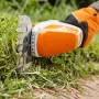 Stihl HSA 26 Akku-Strauchschere schneidet Gras, bedient von Hand mit Handschuh.
