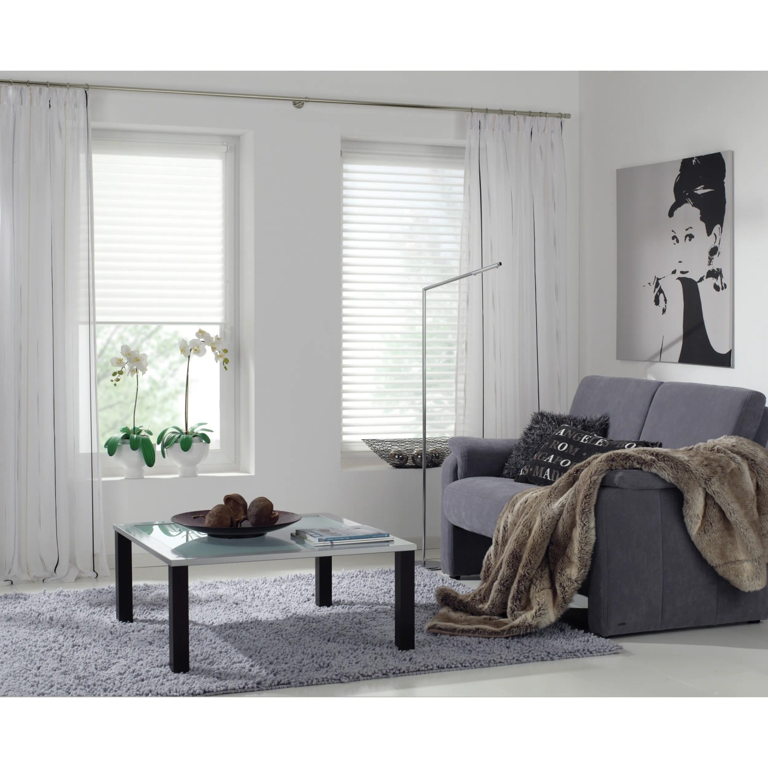 Wohnzimmer mit Gardinenstange, weißen Vorhängen und grauer Couch.