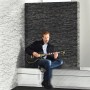 A.S. Creation Vliestapete Naturals Stein Schwarz: Wandgestaltung mit Steinoptik imitiert durch eine Person mit Gitarre.
