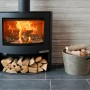 Schwarzer Aduro Kaminofen 15.2 mit Holzscheiten und Korb. Der Kaminofen hat eine Automatik und 6,5 kW Leistung.