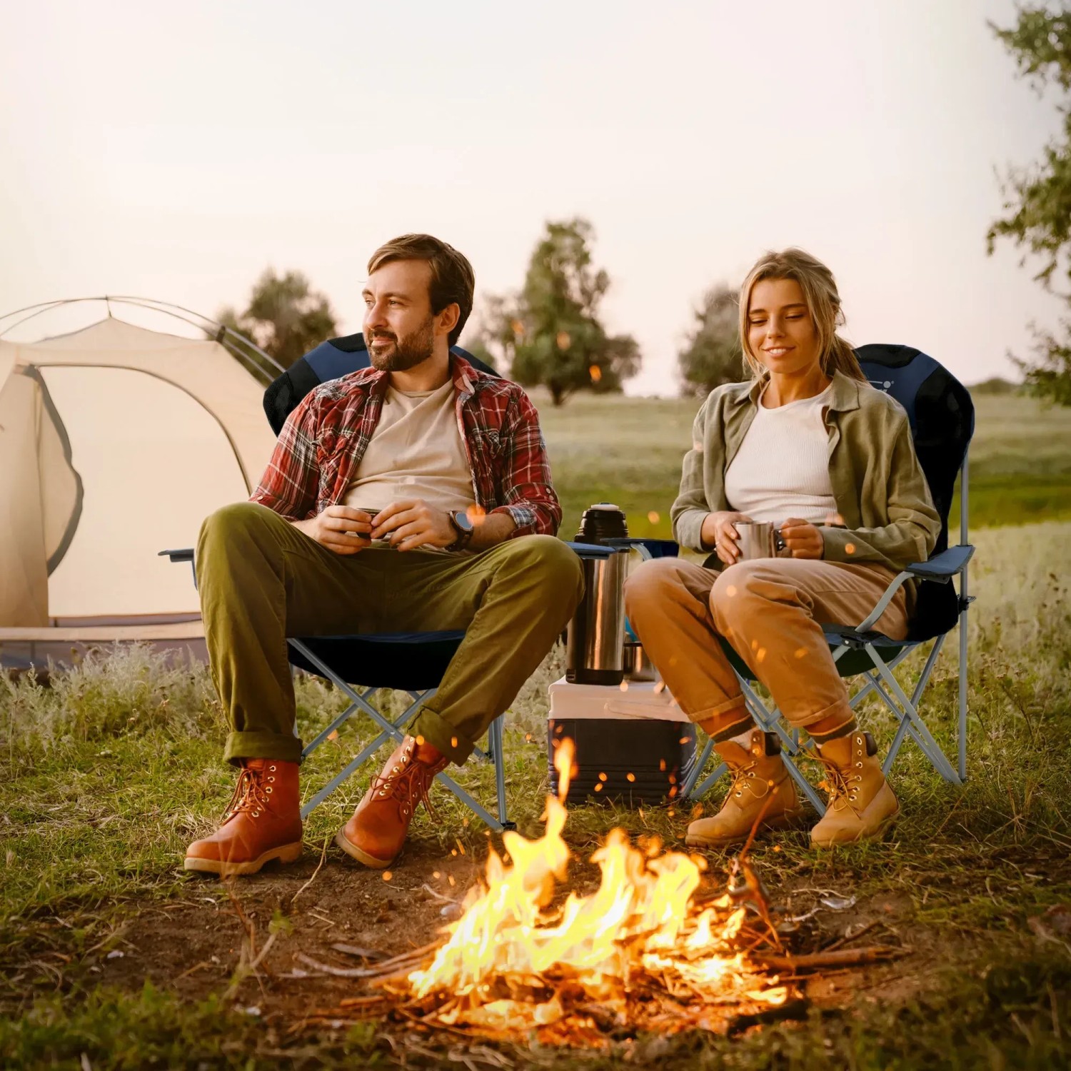 Zwei Personen sitzen in blauen Hauki Campingstühlen am Lagerfeuer. Faltbares 2er-Set, wetterfest bis 150 kg.
