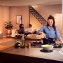 Szene mit Philips Hue White Ambiance E27 LED: Frau kocht, Paar entspannt im Wohnzimmer, warmes Licht.