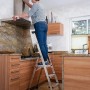 Frau auf Krause Stehleiter Safety Plusline (3 Stufen) in Küche, beim Putzen der Dunstabzugshaube.