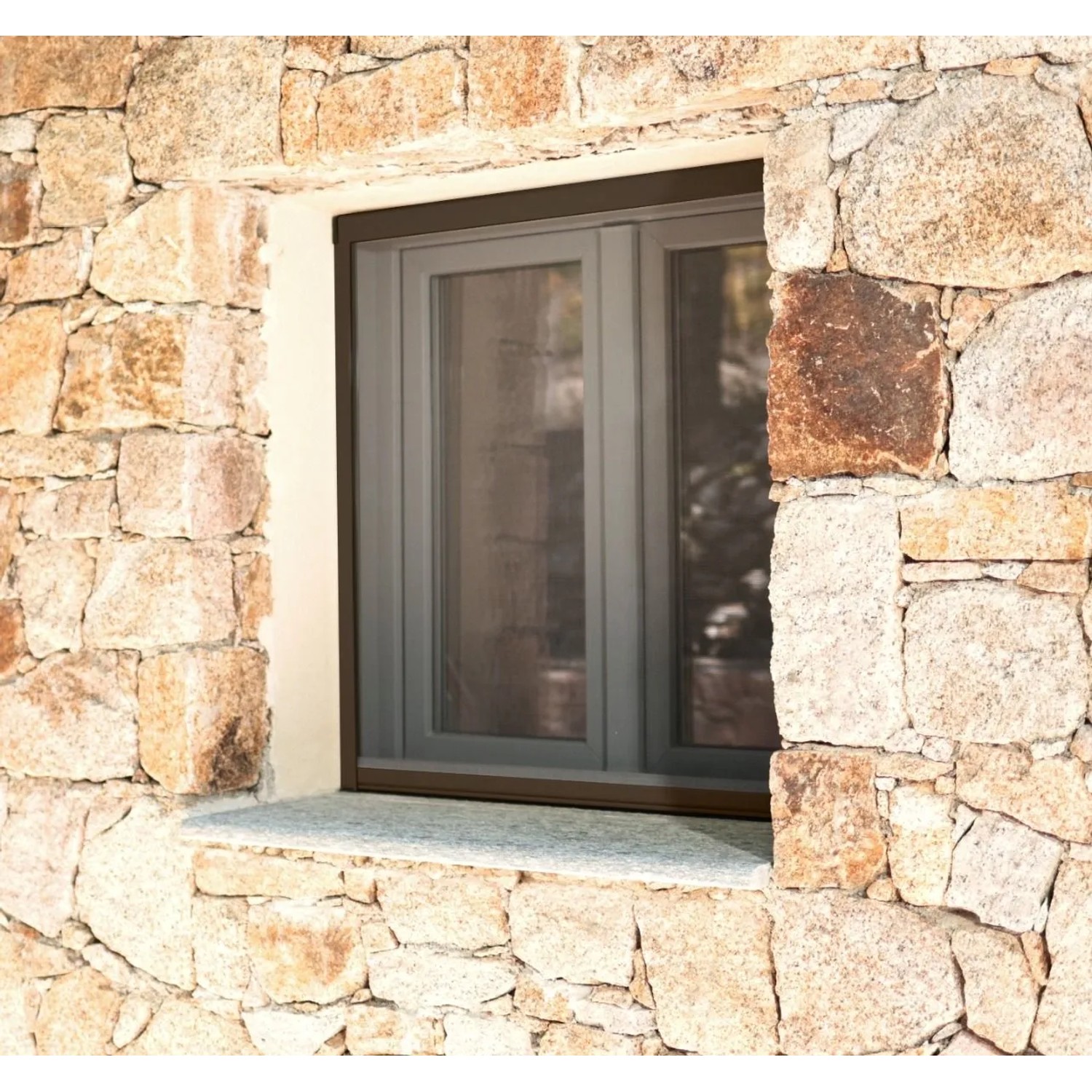 Braunes Avosdim Insektenschutzrollo aus Aluminium am Fenster eines Hauses mit Steinmauer.