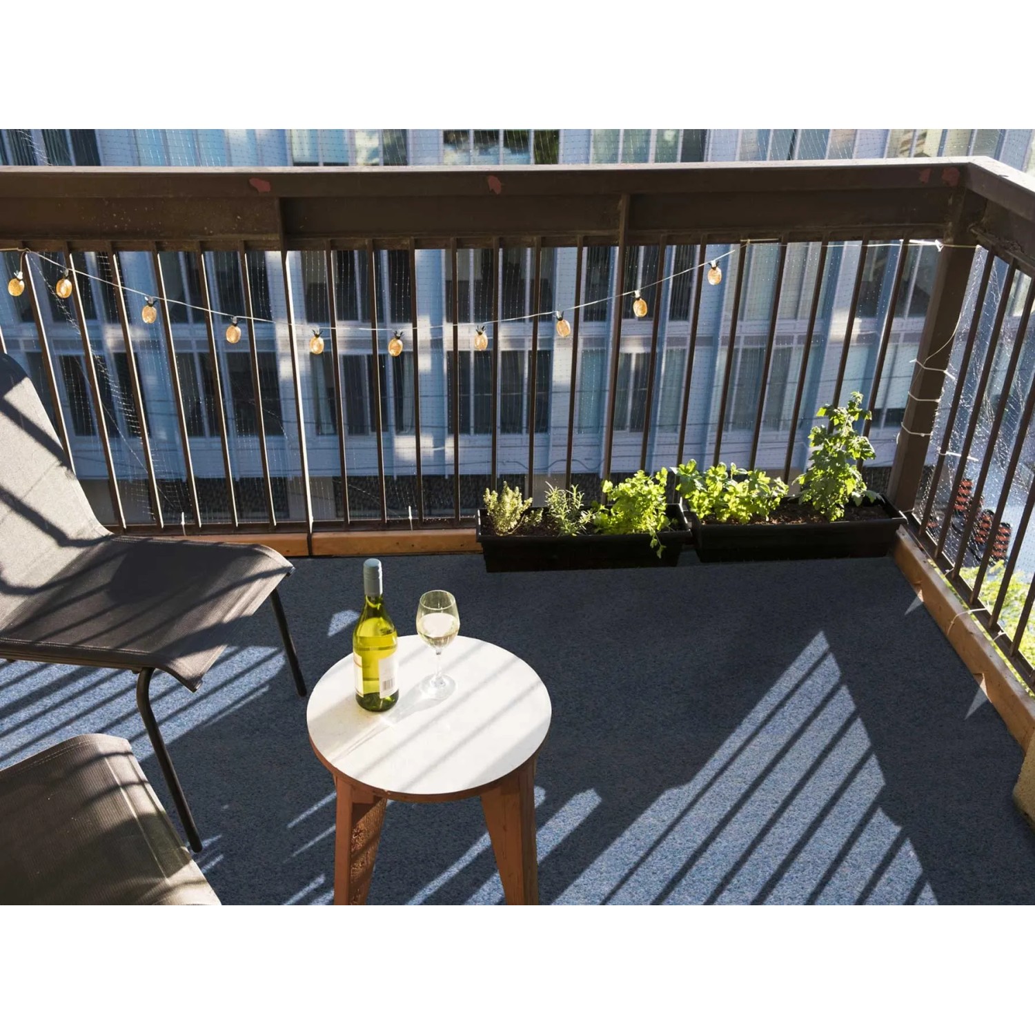 Blauer Primaflor Rasenteppich auf einem Balkon mit Tisch, Stuhl und Pflanzen.