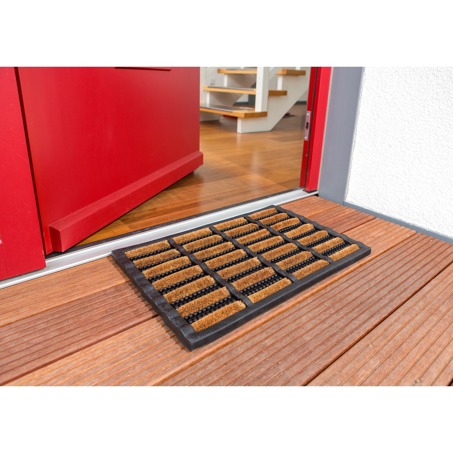 Astra Fußmatte Rimini, 40x60 cm, Design 001, vor roter Haustür auf Holzterrasse.