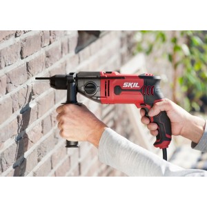 Skil Schlagbohrmaschine 6745GA beim Bohren in eine Ziegelwand, rot/schwarz, mit Zusatzhandgriff.