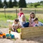 Wendi Toys Sandkasten mit Holzabdeckung und Sitzflächen, bespielt von Kindern im Garten.
