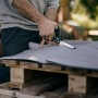 Fiskars Hardware-Schere schneidet graues Material auf Holzpalette. Vielseitige Schere für Haushalt, Garten, Werkstatt.