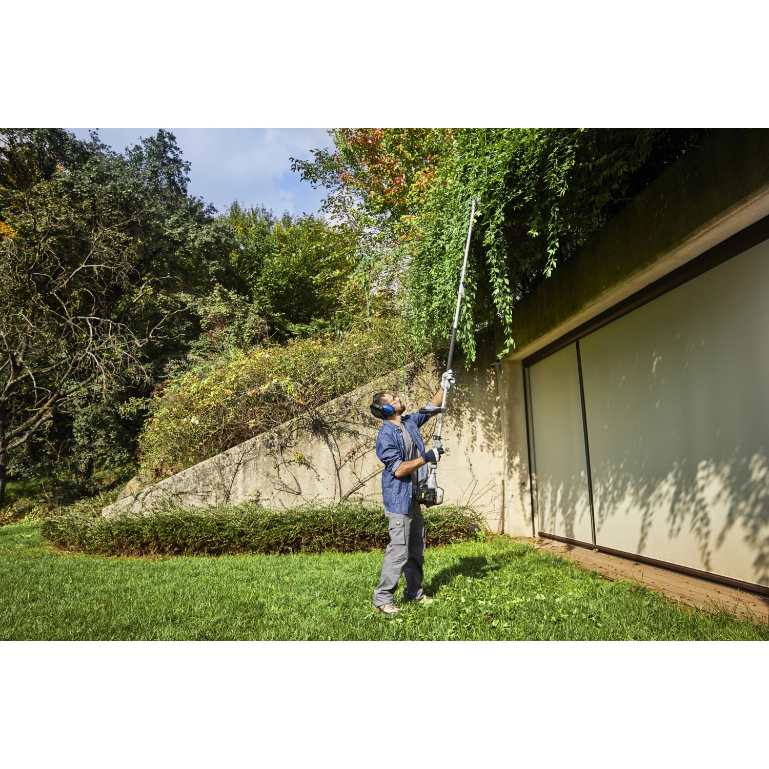 Mann schneidet Hecke mit Alpina Benzin-Multi-Tool AMT 26 5 in 1 Hochentaster.