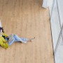Frau liest auf Kaindl Poseidon Laminatboden in Tahiti Oak Optik nahe Fenster und Sofa.