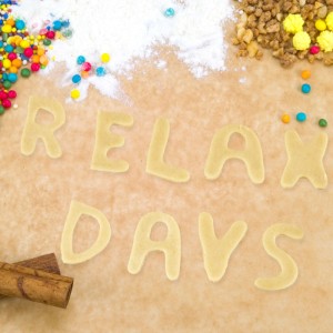 Edelstahl Plätzchen Ausstecher Set. Teigbuchstaben RELAX DAYS, umgeben von Streuseln und Zimtstangen. Ideal für Backen.