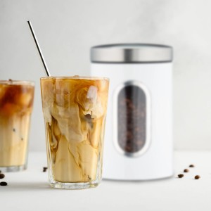 Graue Relaxdays Vorratsdose aus Metall mit Sichtfenster neben Eiskaffee.