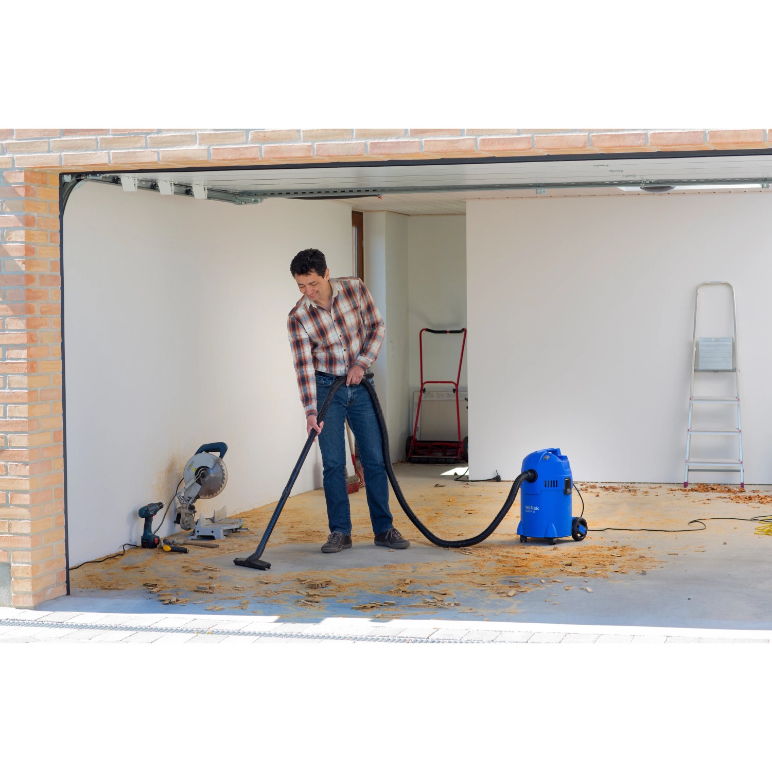 Mann saugt mit blauem Nilfisk Nass- und Trockensauger Buddy II 18 eine Garage.