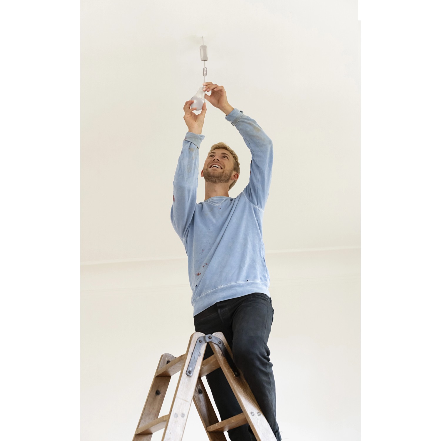 Mann wechselt LEDVANCE 10W Energiesparlampe in Glühlampenform auf einer Leiter.