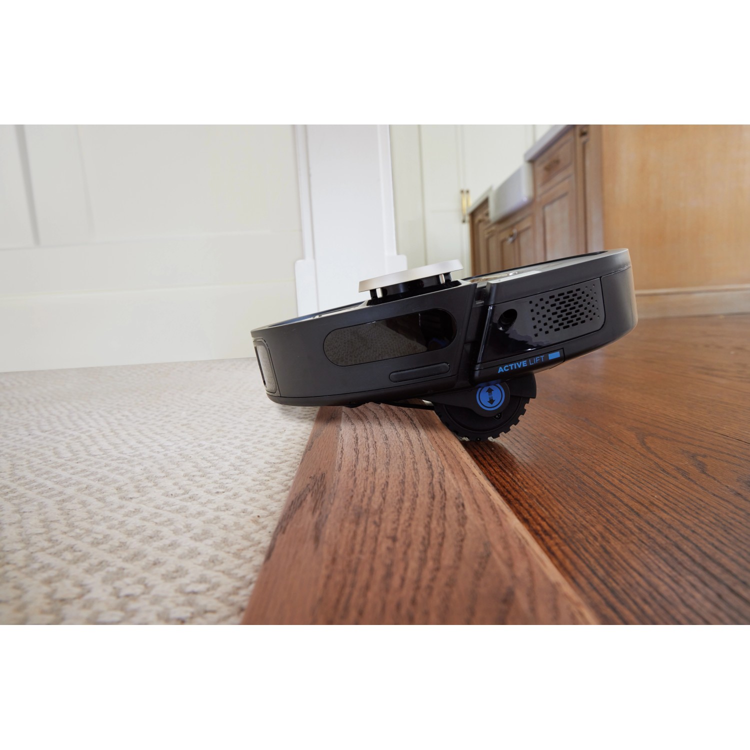 Shark Saugroboter Power Detect überwindet eine Türschwelle zwischen Teppich und Holzboden.