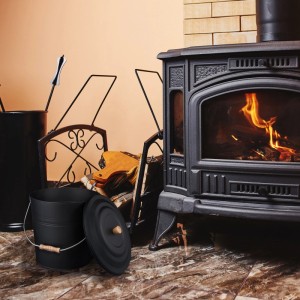 Schwarzer Relaxdays Ascheeimer aus Stahl, 12 l, mit Deckel und Holzgriff neben Kaminofen.