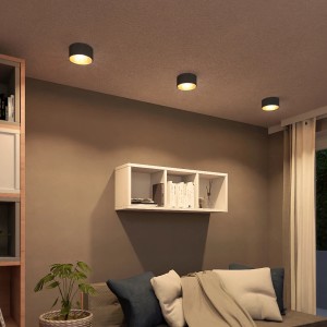 Drei schwarze LED Aufbaustrahler mit goldener Innenseite an einer Decke über einem Wohnbereich.