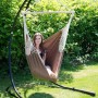 Brauner AMANKA Hängesessel aus Baumwolle mit Holzstab. Frau entspannt im Garten auf schwarzem Gestell.