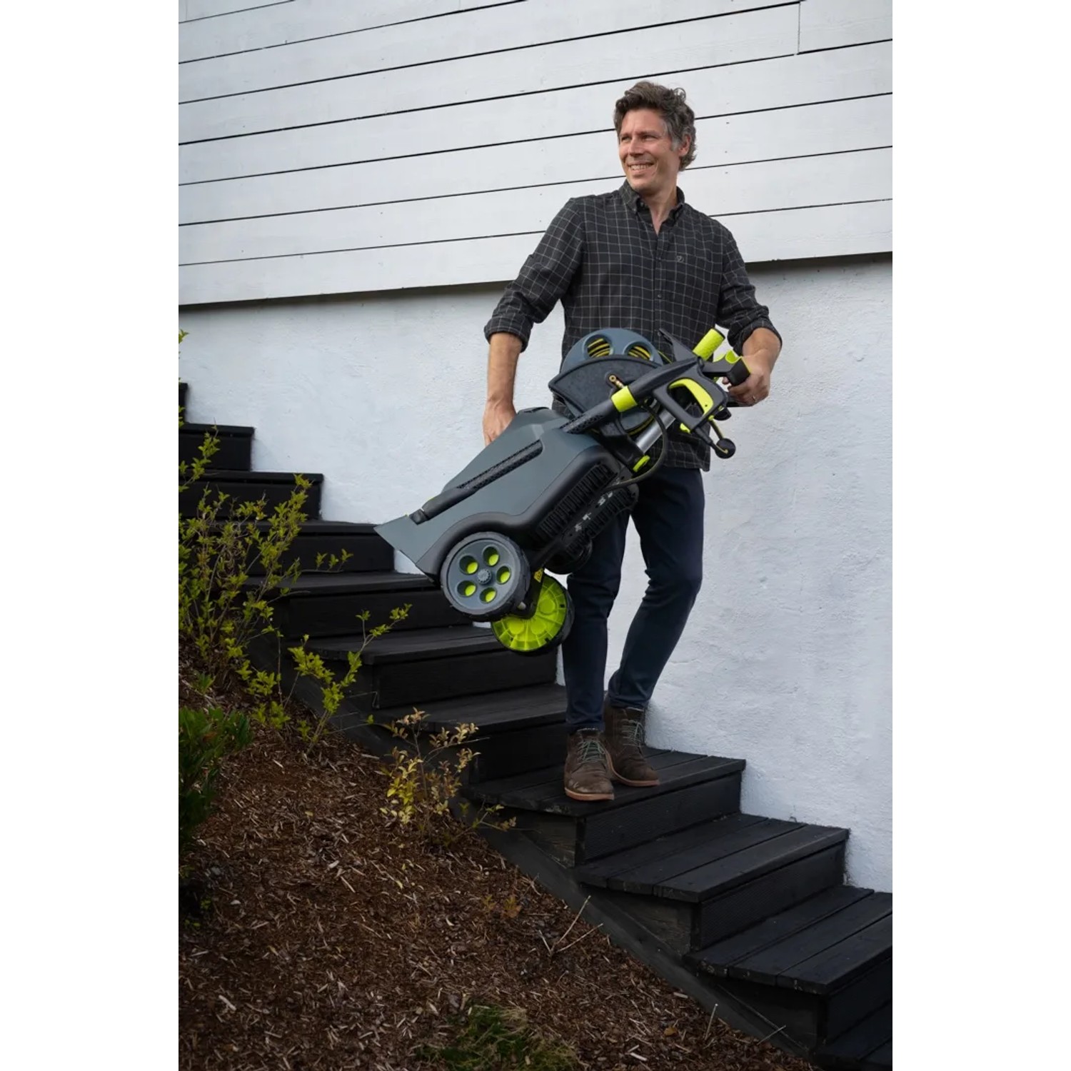AVA Evolution P60 Hochdruckreiniger, getragen auf Treppe. Graues Gehäuse, grüne Räder und Zubehör.