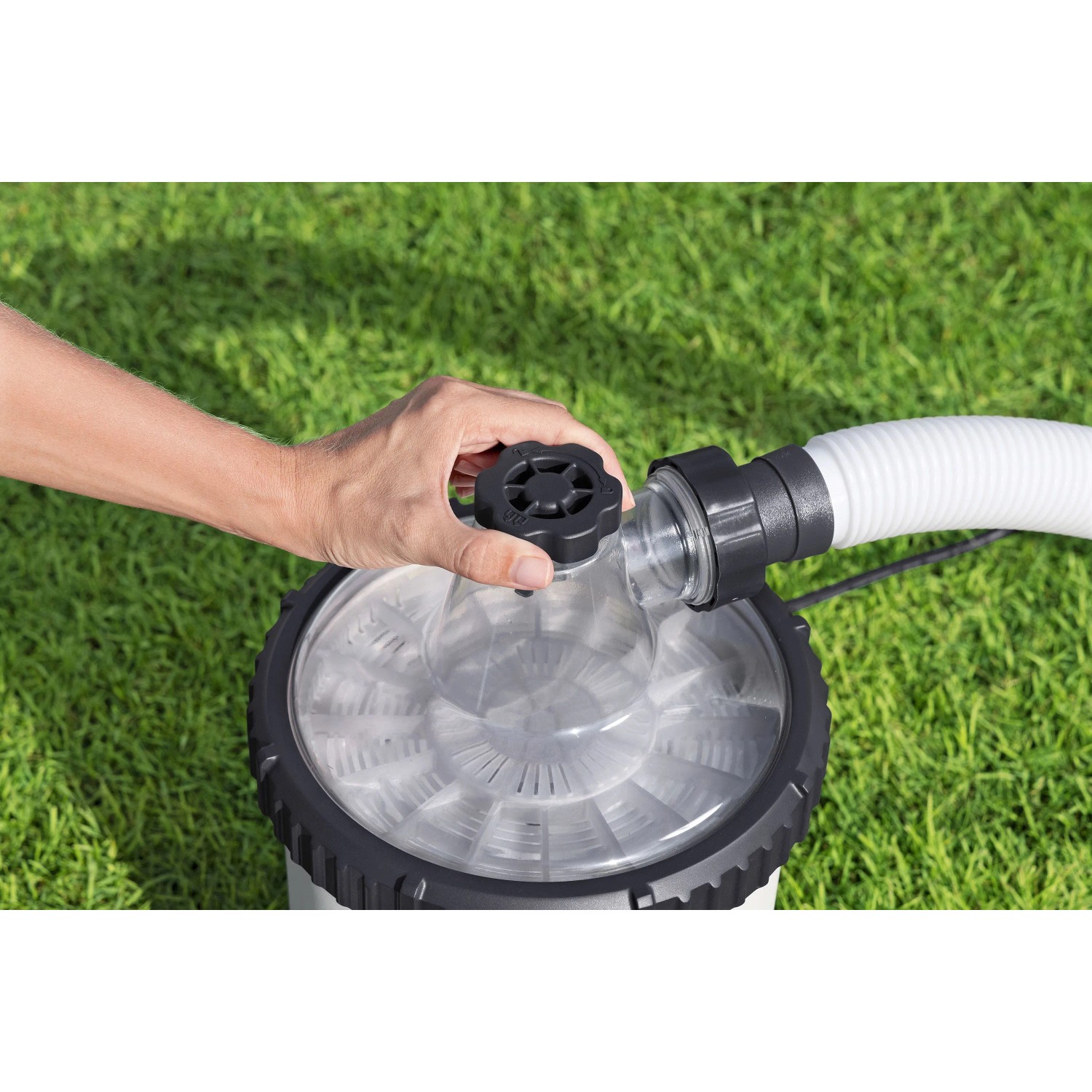 Hand dreht Regler an Bestway Polysphere Filterpumpe mit weißem Schlauch auf Rasen. Pool Filtermedien für klares Wasser.