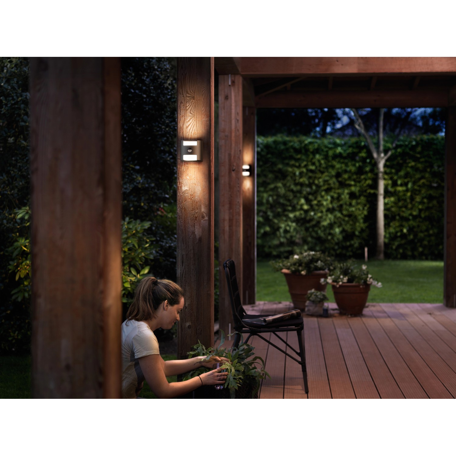 Philips LED-Außenwandleuchte Grass Anthrazit an Holzpfosten, warmweißes Licht.