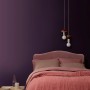 Schlafzimmer mit ELLE DECORATION Wandfarbe Pigment No. 472 (matt) in Lila. Bett mit rosa Tagesdecke.