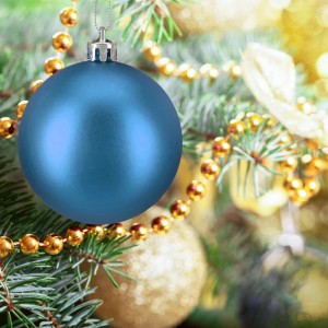 Eine glänzende petrolfarbene Weihnachtskugel aus Kunststoff hängt am Christbaum.