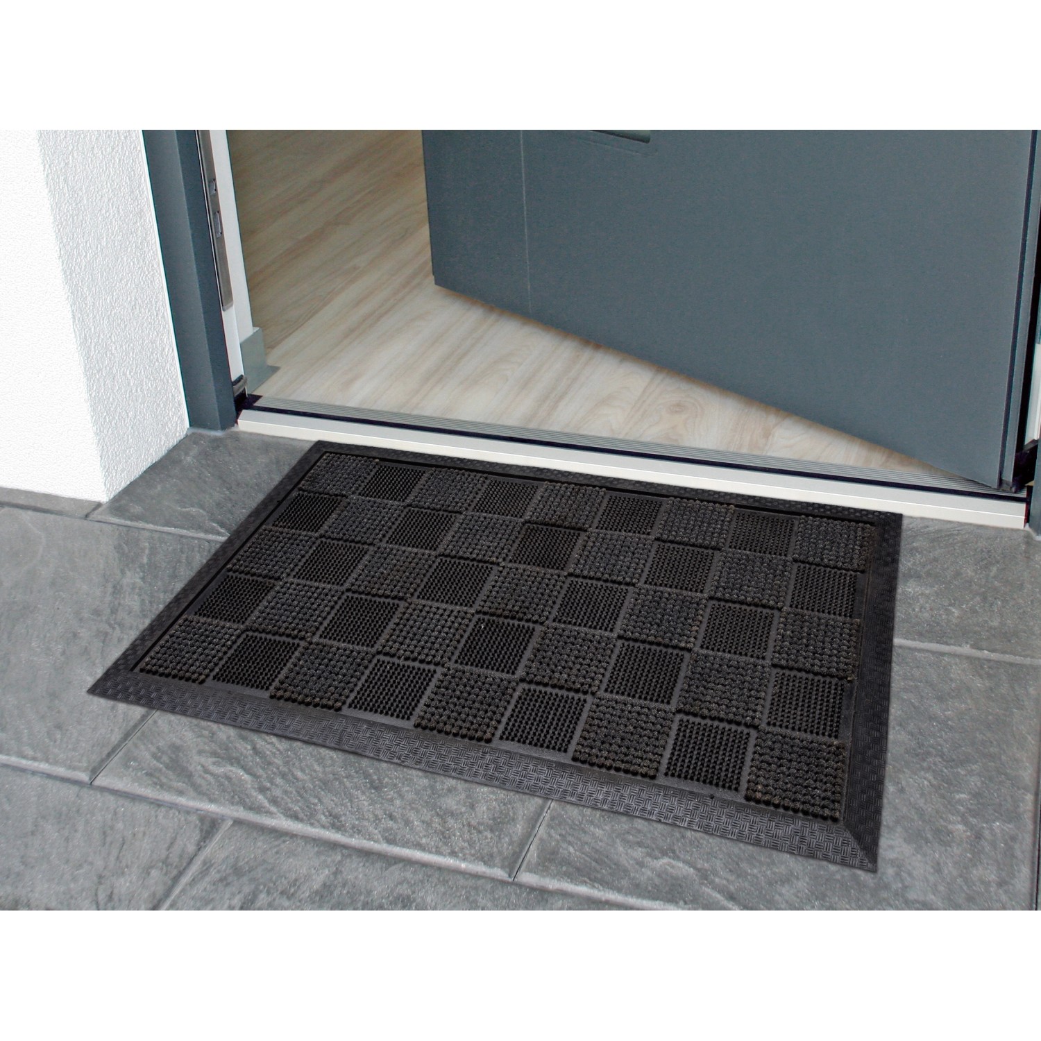 Schwarze Gummipinmatte 40x70 cm mit Beflockung vor einer Tür, ideal für den Außenbereich.