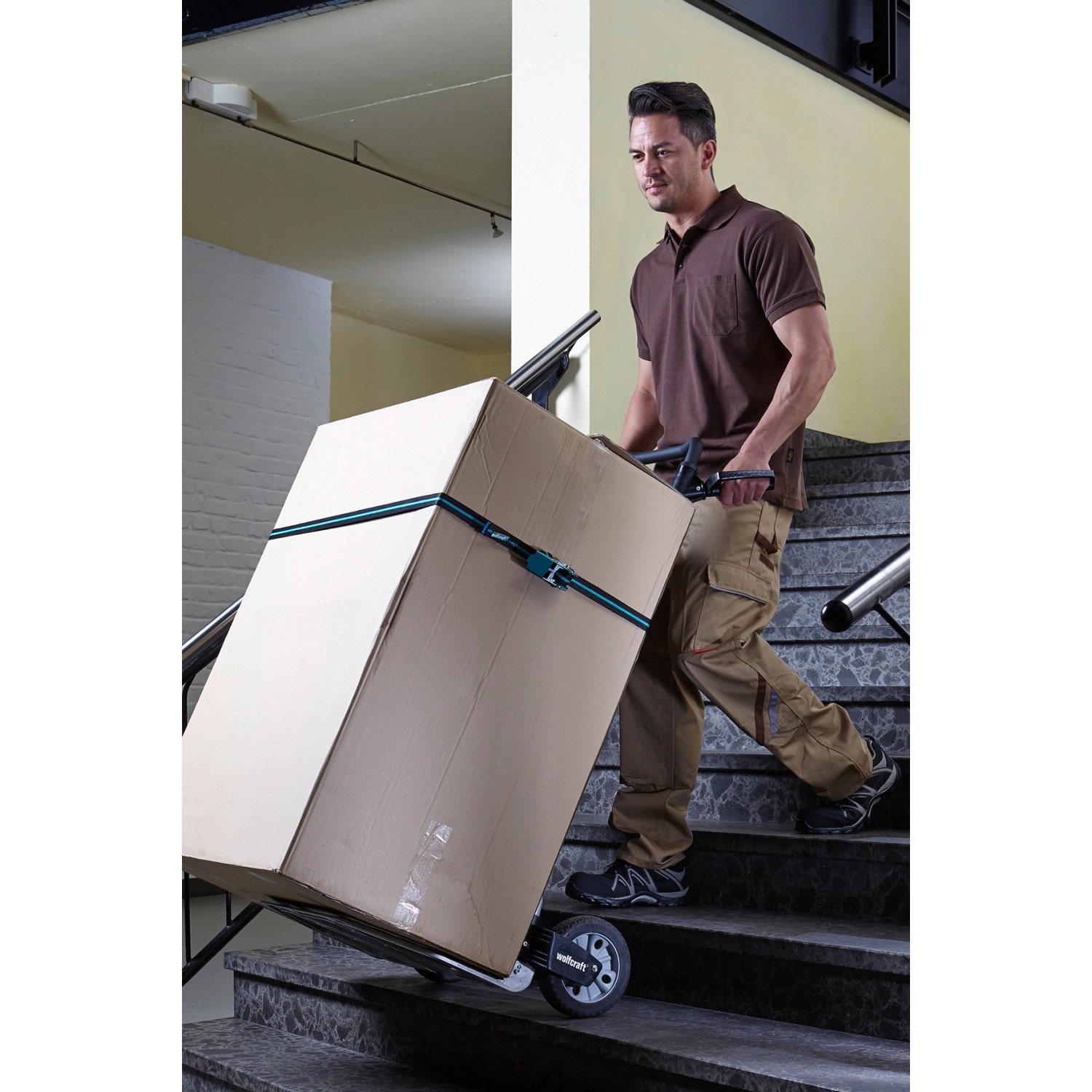 Mann transportiert Karton mit klappbarer wolfcraft Sackkarre TS 1500 auf Treppe.