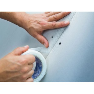 Hände kleben weißes LUX-TOOLS Fugenband 50 mm auf Gipskartonwand. Für stabilen Trockenausbau, verhindert Risse.