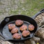 Petromax Feuerpfanne FP30-T: Gusseisenpfanne (Ø 30cm) mit Stiel und Bratlingen auf offenem Feuer.