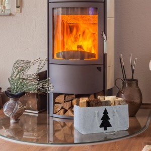 Hellgraue Relaxdays Kaminholztasche aus Filz mit Tannenbaum-Motiv vor Kamin.