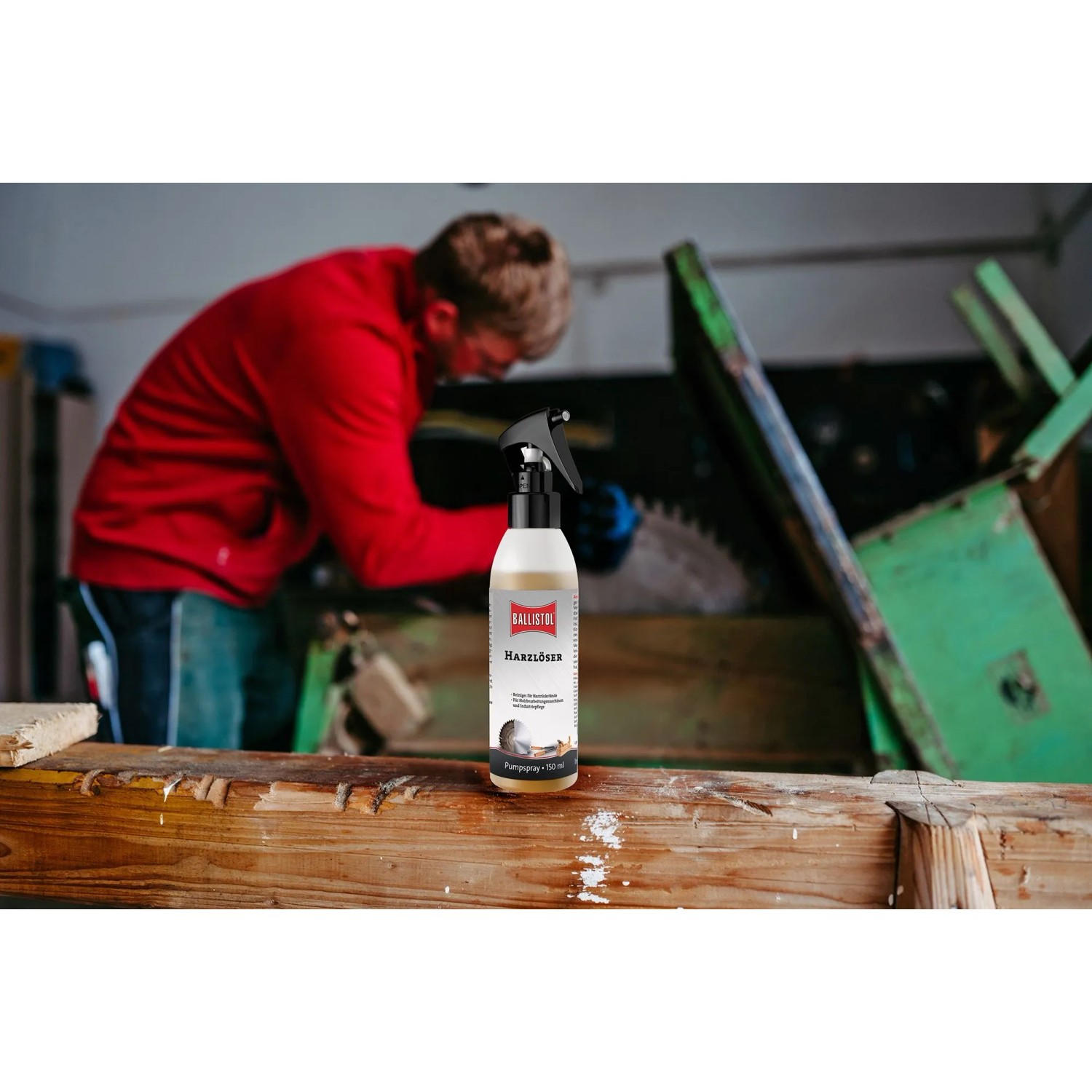 Ballistol Harzlöser Pumpspray 150 ml auf Holzbalken, im Hintergrund ein Handwerker an einer Säge. Entfernt Harz von Werkzeugen.