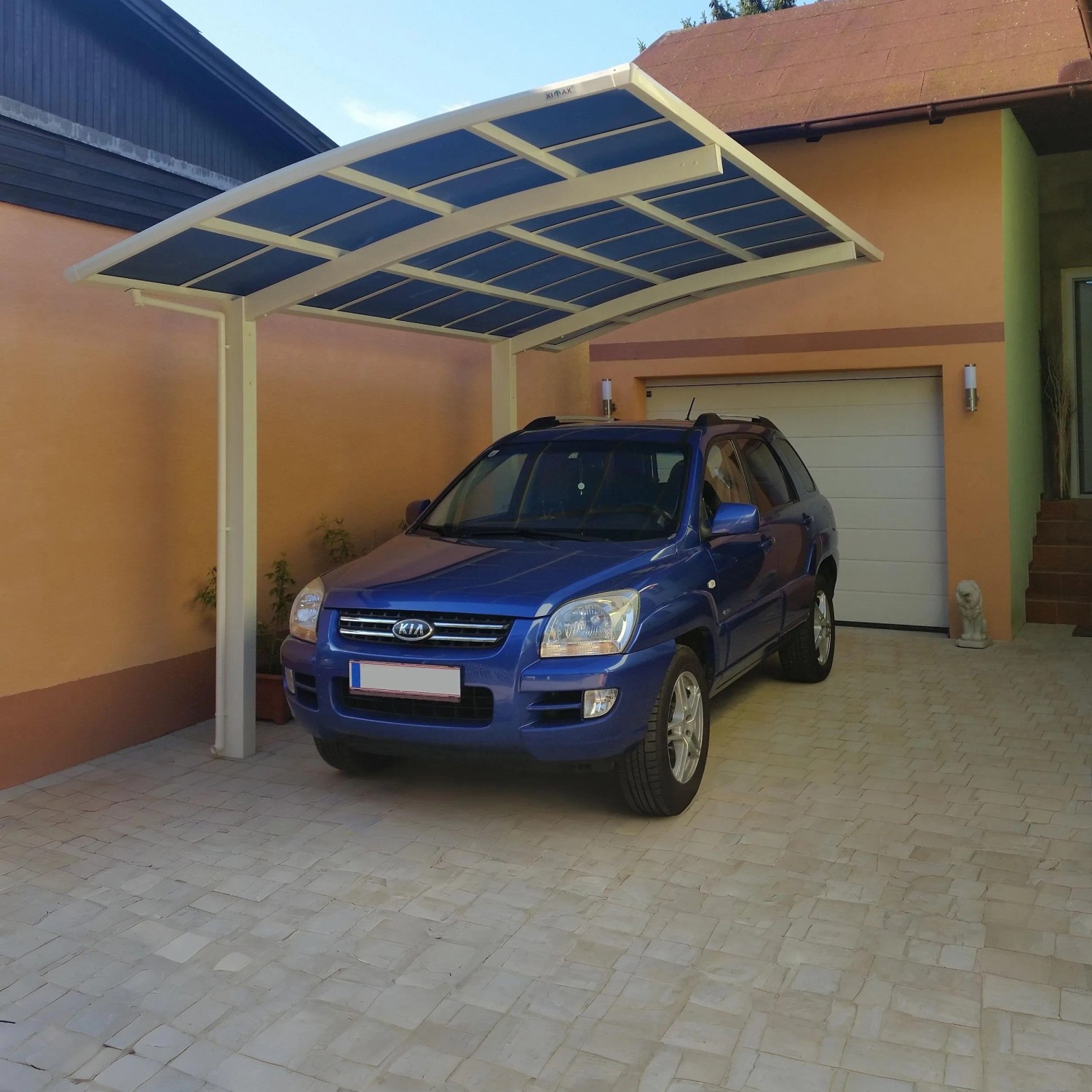 Winterweißer Ximax Carport Portoforte-80 mit blauem Auto darunter. Moderner Metallcarport mit gebogenem Dach.