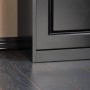 Detailaufnahme: Schwarzer Schuhkipper mit Klappe und Sitzkissen auf dunklem Holzboden.