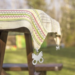 Silberner Schmetterling Tischdeckenbeschwerer aus Edelstahl an gemusterter Tischdecke im Garten. Ideal für Outdoor-Tische.