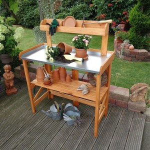 Klappbarer Pflanztisch aus Holz mit verzinkter Arbeitsfläche und Ablagen für Gartenzubehör.