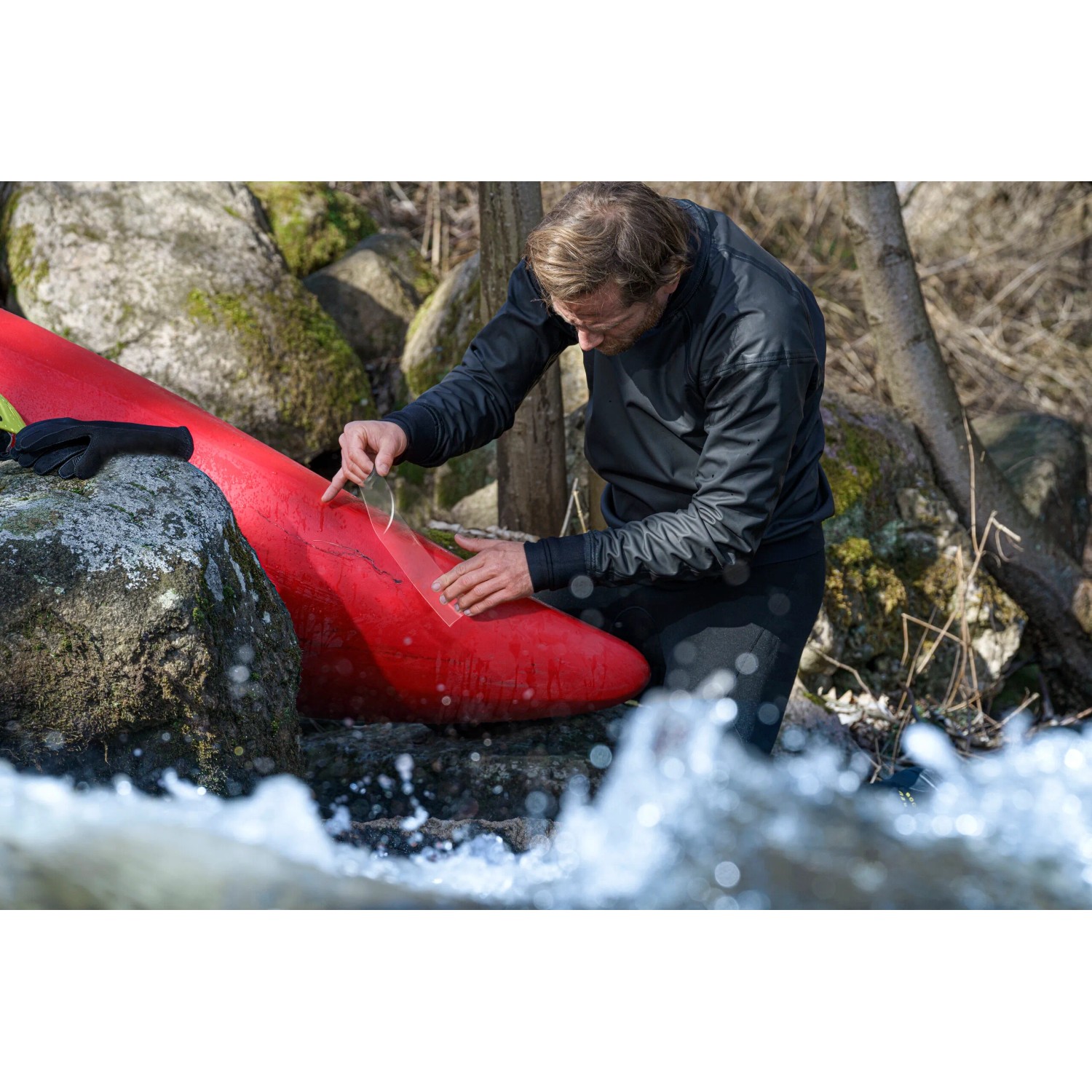 Mann repariert rotes Kajak mit transparentem Tesa Reparaturband Ultra Power Under Water im Freien.