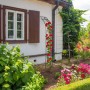 Schwarzer Rosenbogen aus Eisen zur Wandmontage mit roten Rosen vor weißer Hauswand.