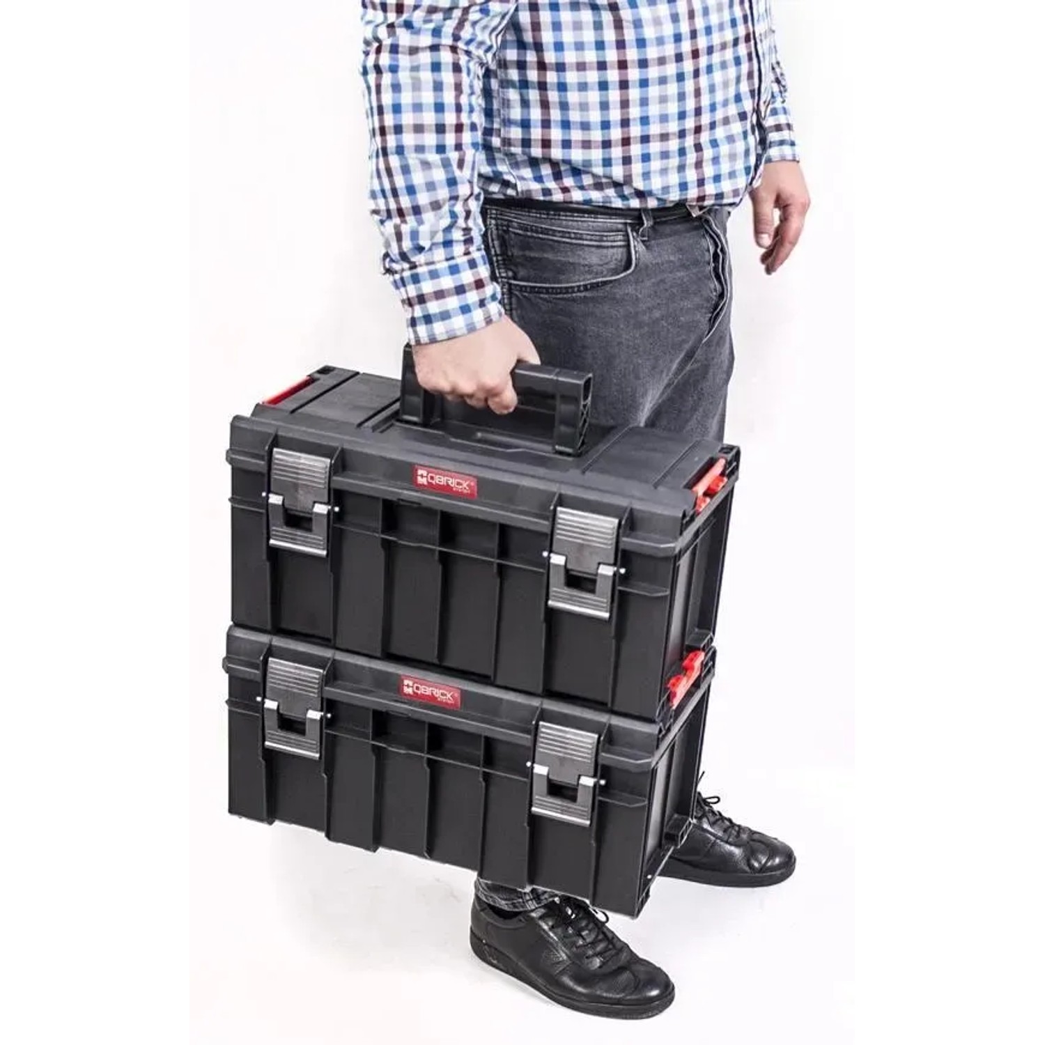 Mann trägt zwei schwarze PROREGAL QBRICK Werkzeugkoffer mit Klemmverschlüssen.
