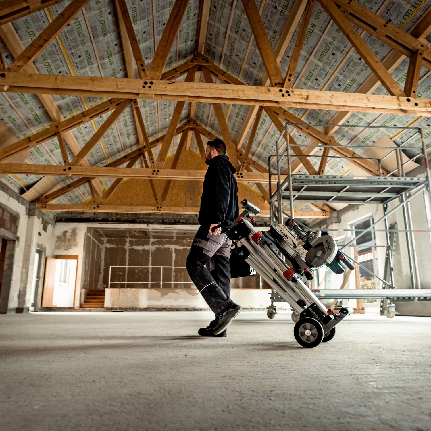 Mann transportiert Metabo Kapp- & Zugsäge KGS 254 M auf einem Rollwagen in einer Baustelle.