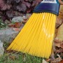 Sonneck Universalbesen mit gelben Borsten und Stiel im Einsatz auf Rasen und Laub.