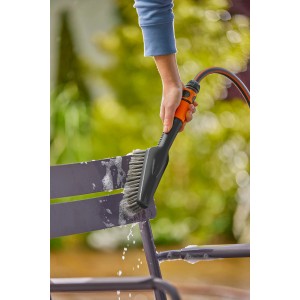 Gardena Cleansystem Handbürste Soft S mit Schlauchanschluss im Einsatz zur Reinigung eines Gartenstuhls.