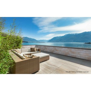 Terrasse mit EHL Mauerstein Tribus CityPur in Sandstein-Nuanciert und Lounge-Möbeln vor Seelandschaft.