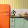 ESTAhome Vliestapete mit gelben Streifen an einer Küchenwand, kombiniert mit orangefarbenem Kühlschrank.
